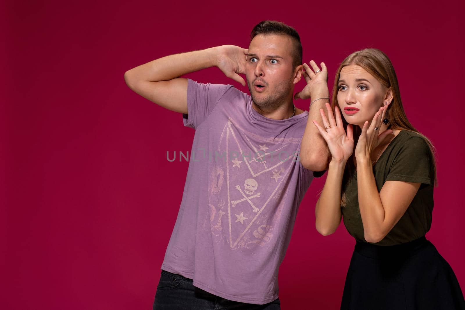 Unhappy discontent woman and man look with disgusting expression, as see something unpleasant. Friends express negative emotions and feelings, isolated over burgundy background. Awkward couple