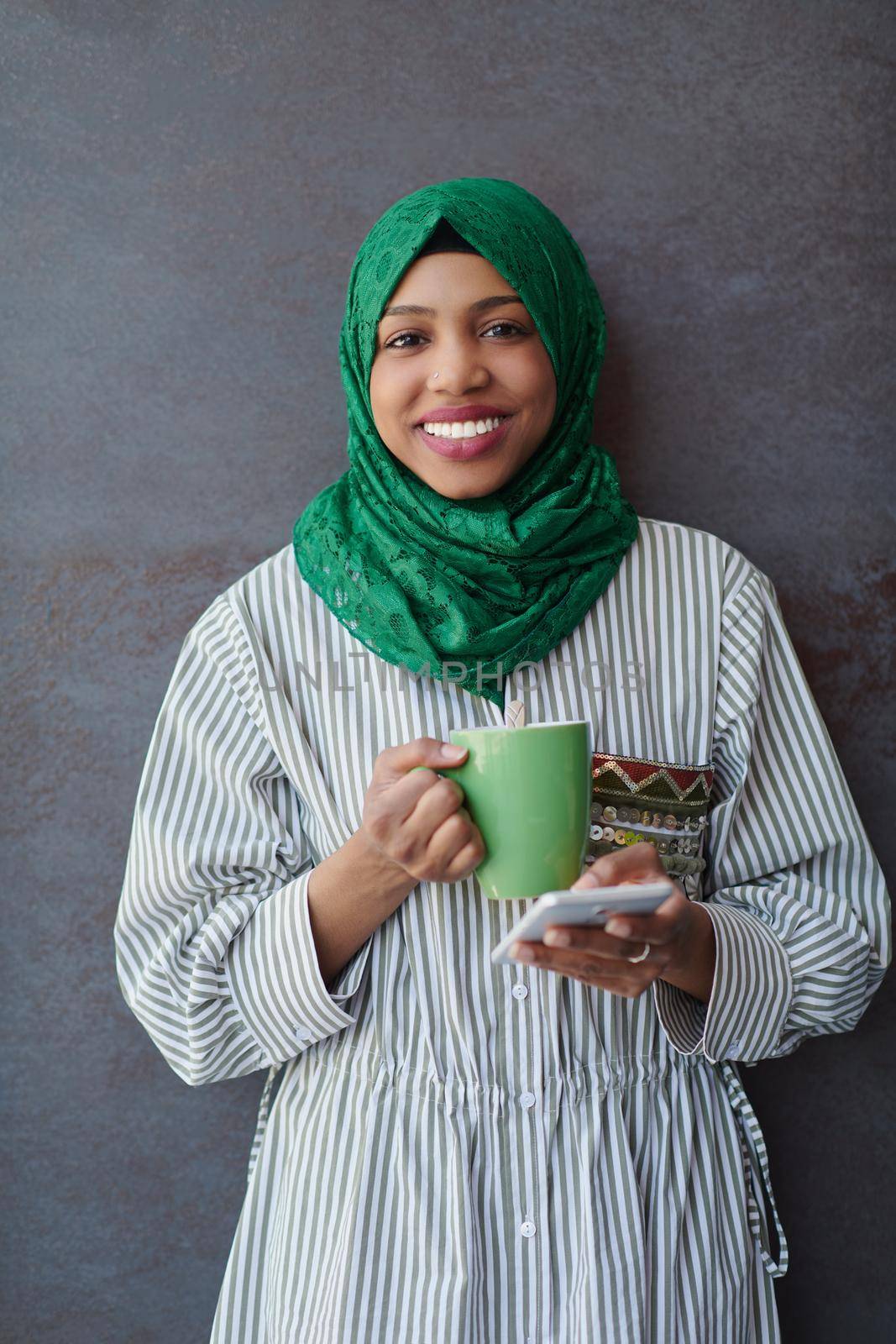 african muslim businesswoman with green hijab using mobile phone during coffee break from work in front of gray wall outside