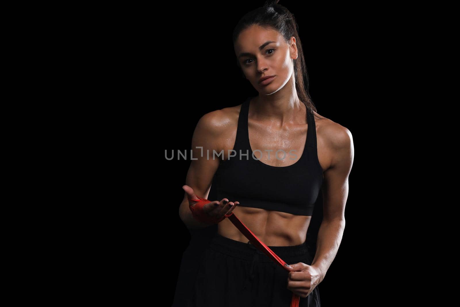 Beautiful and fit female fighter getting prepared for the fight or training, wrapping her hands with bandage tape against dark background