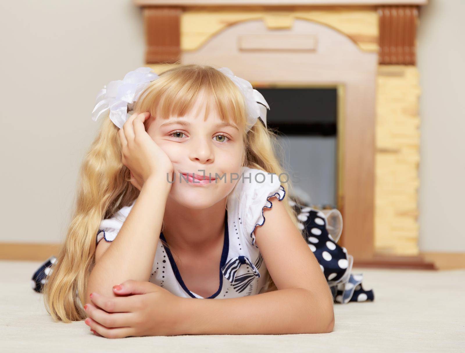 Cute little girl dressed in polka-dot dress lies near the fireplace