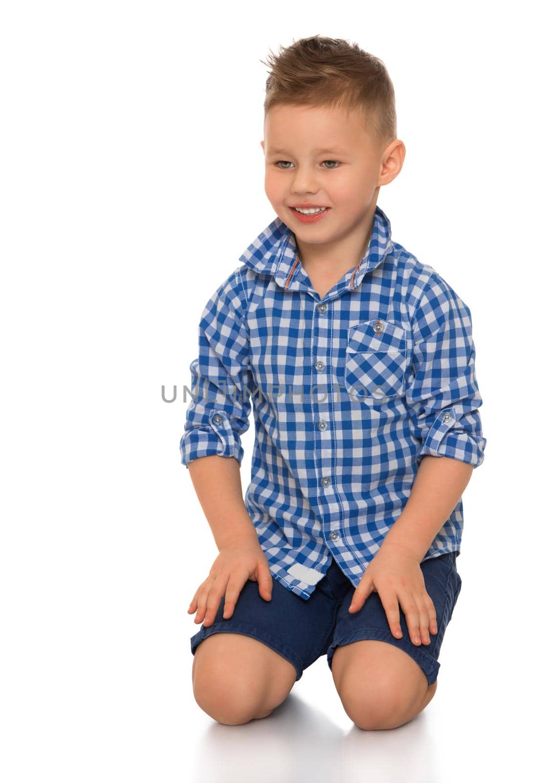 Beautiful little boy in shirt with short sleeves and shorts. The boy sits on the floor. - Isolated on white background
