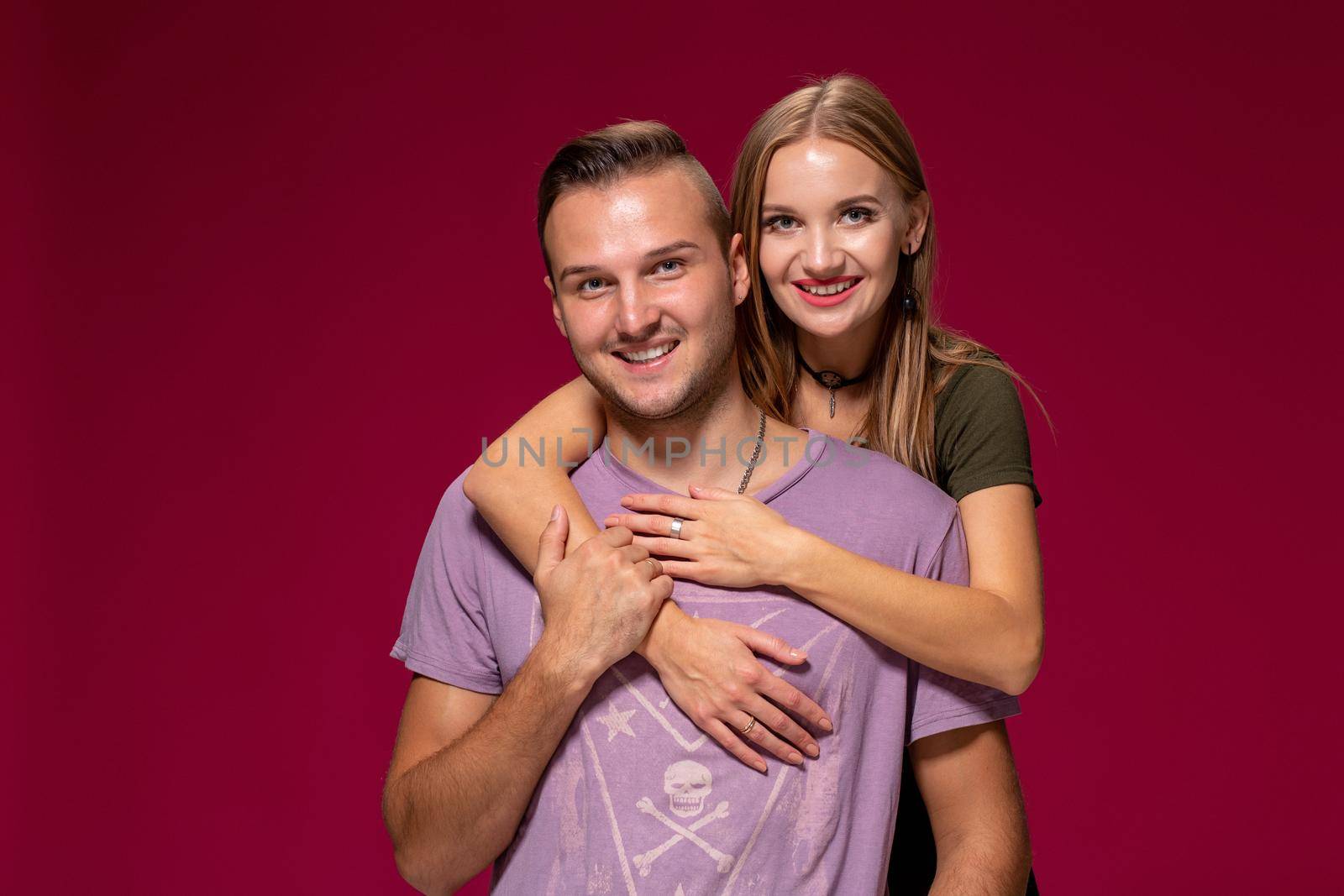 Young nice couple posing in the studio, express emotions and gestures, smiling, on a burgundy background with copy space for your advertisement or written text.