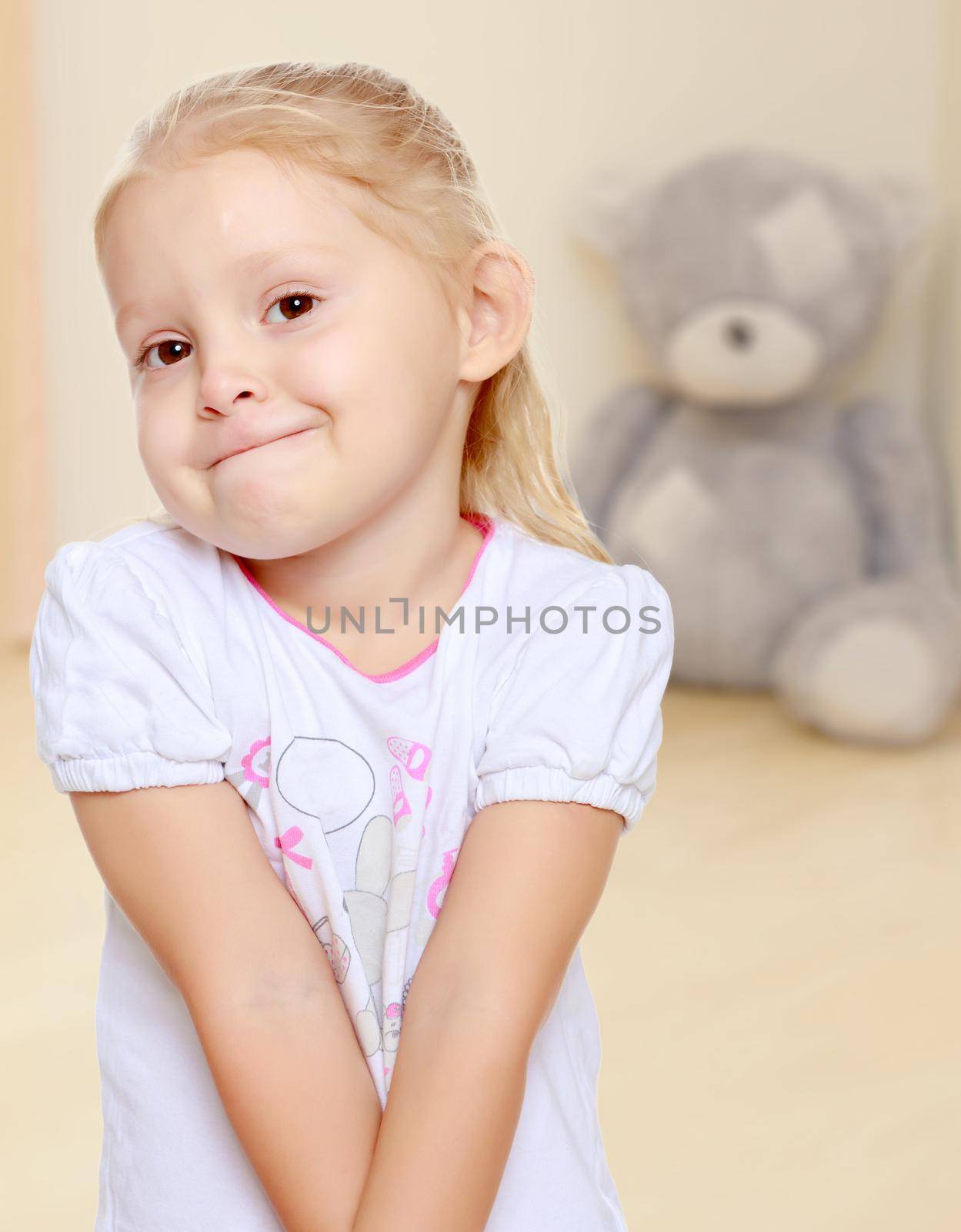 The concept of preschool development of the child ,against a child's room where in the background a Teddy bear.Delicate little blonde girl in a white t-shirt.