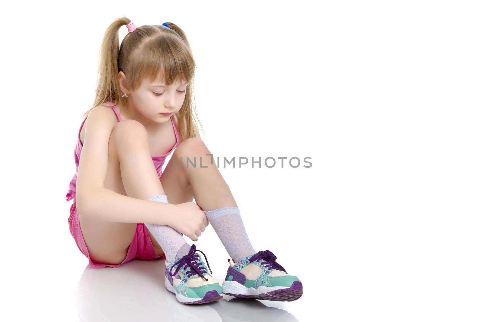 A sweet little gymnast girl is upset, she sits on the floor and cries. The concept of sport, children's emotions. Isolated on white background.