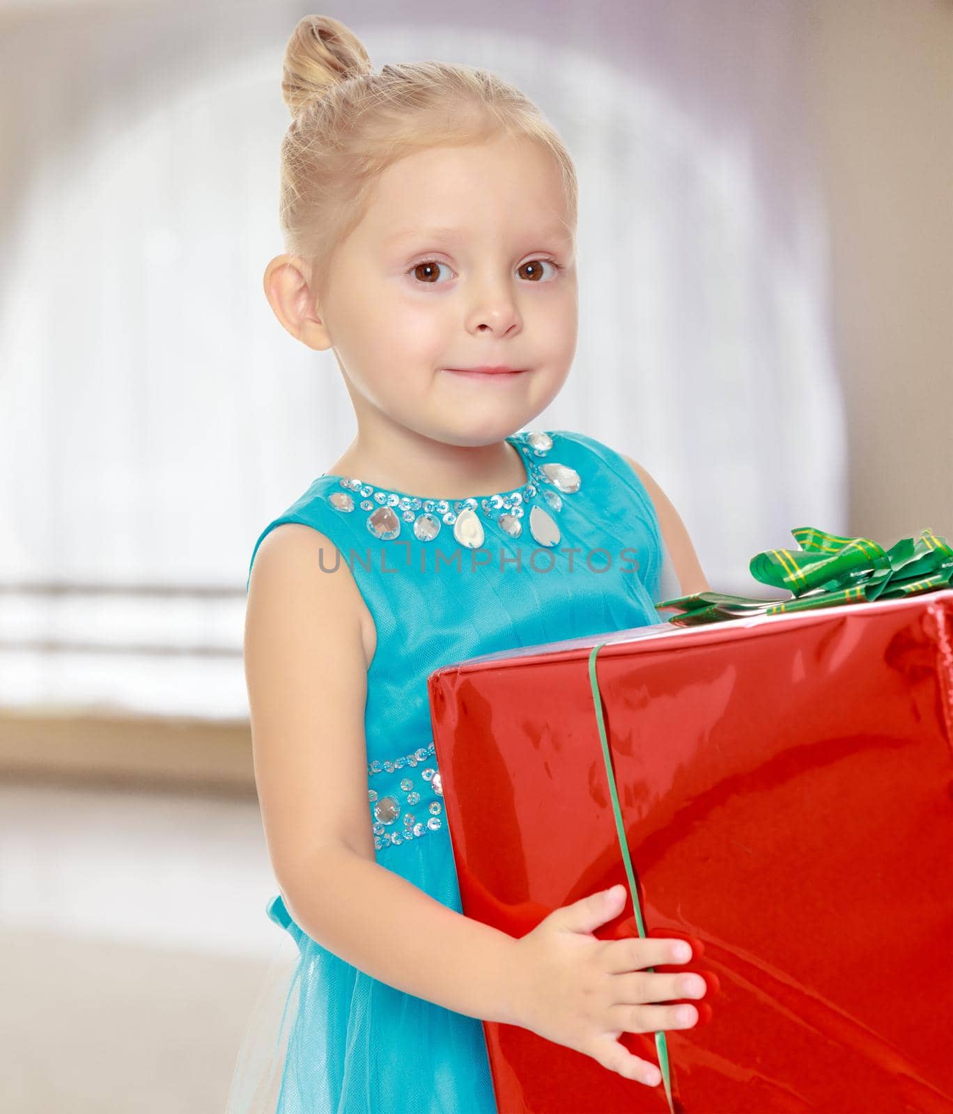 Caucasian little girl in a blue dress, holding the hands of the big red box that is a gift.Girl holding a box in front of him.