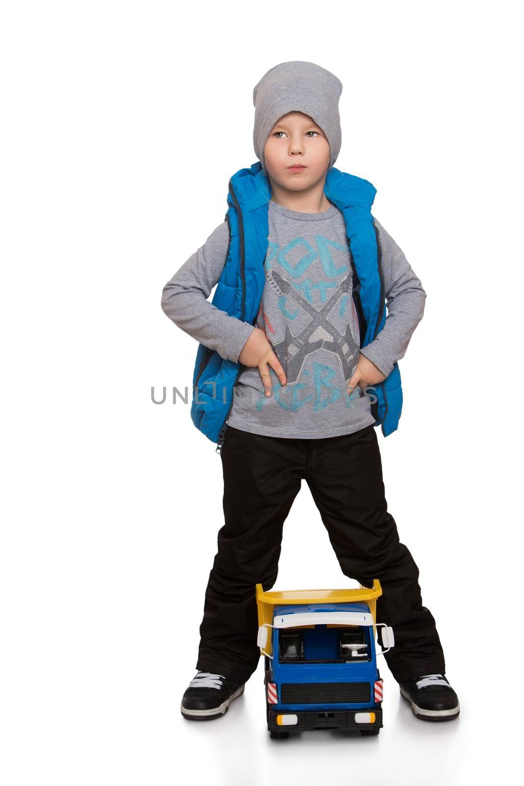 Beautiful little boy in the autumn is to walk on the street in warm pants , a jacket and a cap. A boy plays with a machine - Isolated on white background