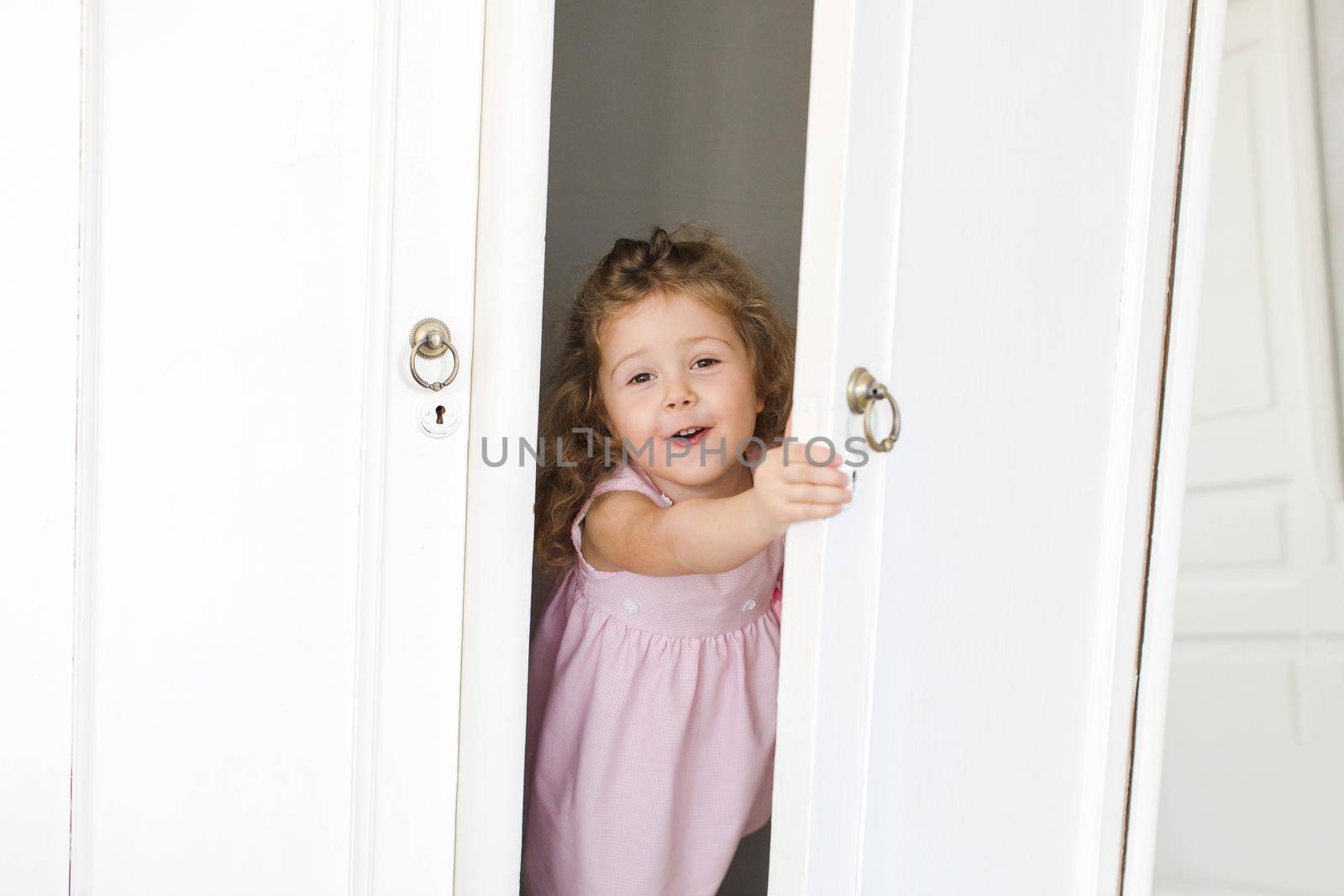 Adorable little girl hiding and looking out of wooden wardrobe.