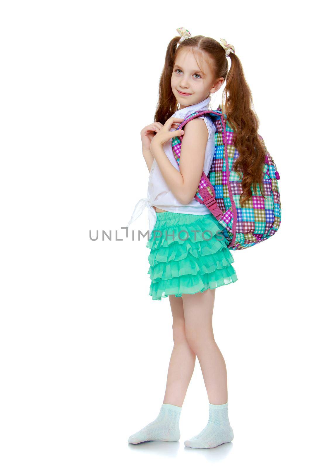 Cute little girl with long hair to the waist which wire braided white ribbons. In a white shirt without a pattern and green short skirt. The girl holds the shoulders schoolbag -Isolated