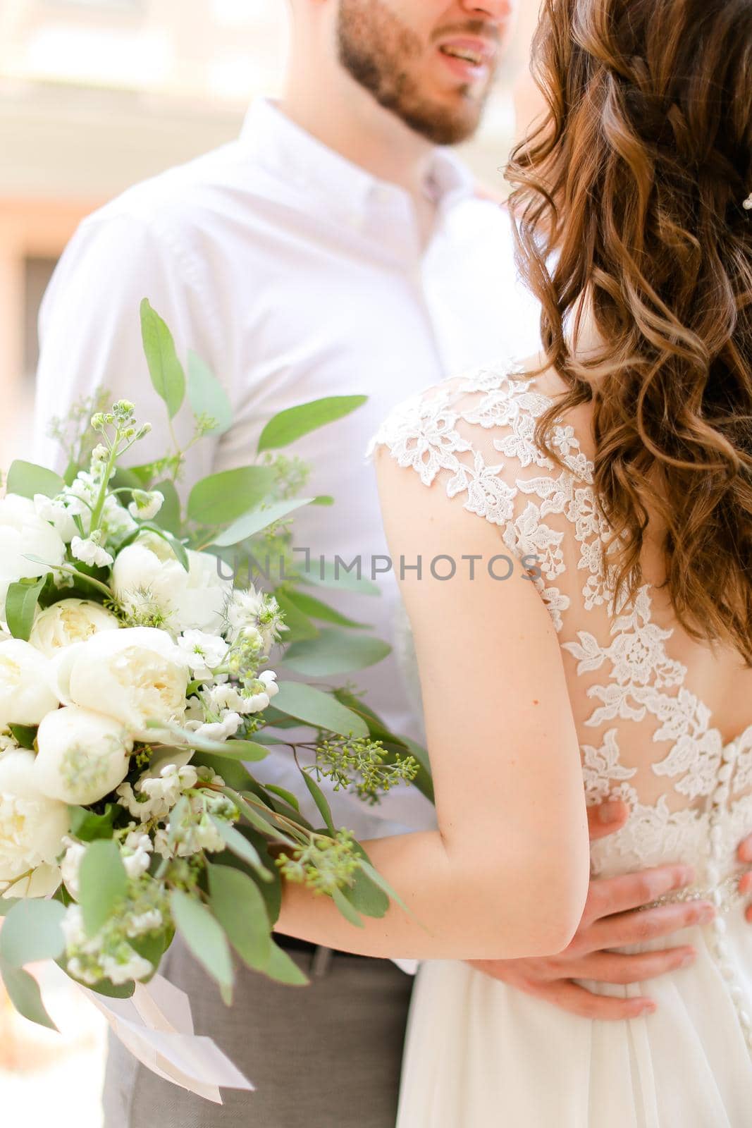Happy european groom kissing bride keeping bouquet of flowers. Concept of love and wedding photo session.