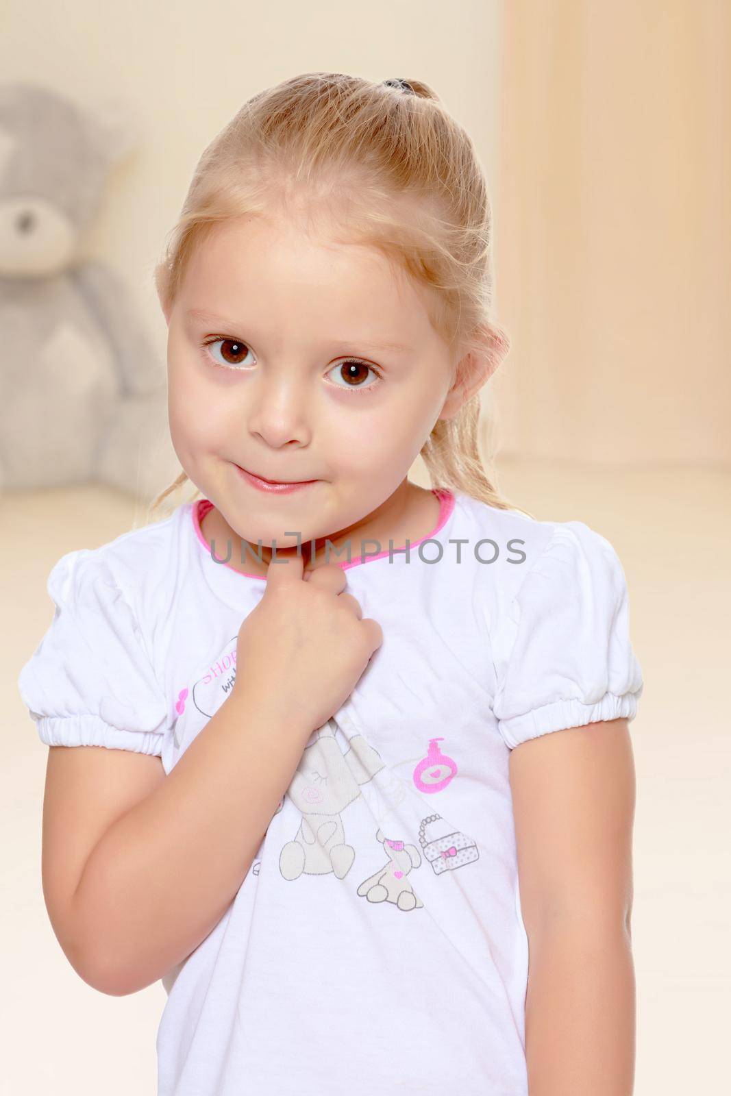 Delicate little blonde girl in a white t-shirt.The concept of preschool development of the child ,against a child's room where in the background a Teddy bear.