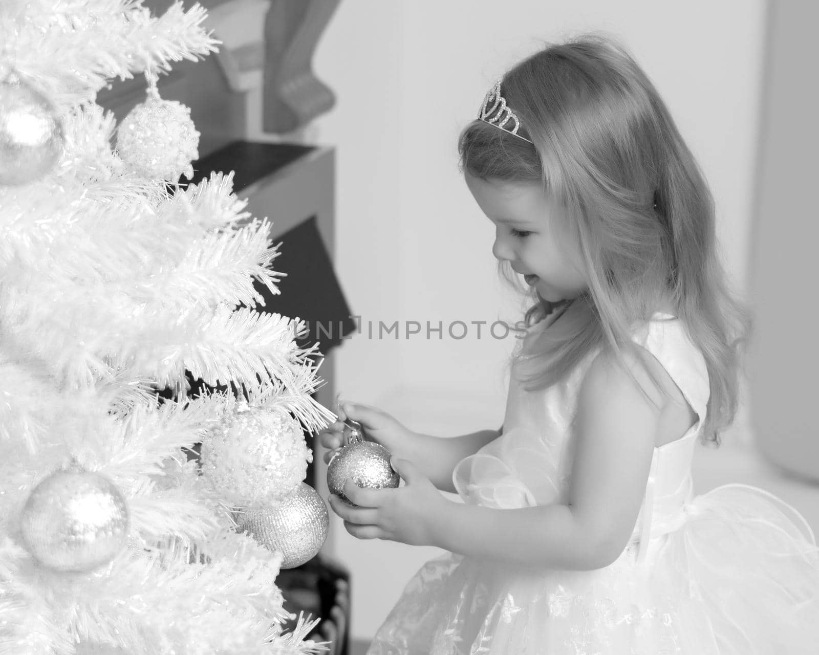 A little girl is decorating a Christmas tree. by kolesnikov_studio