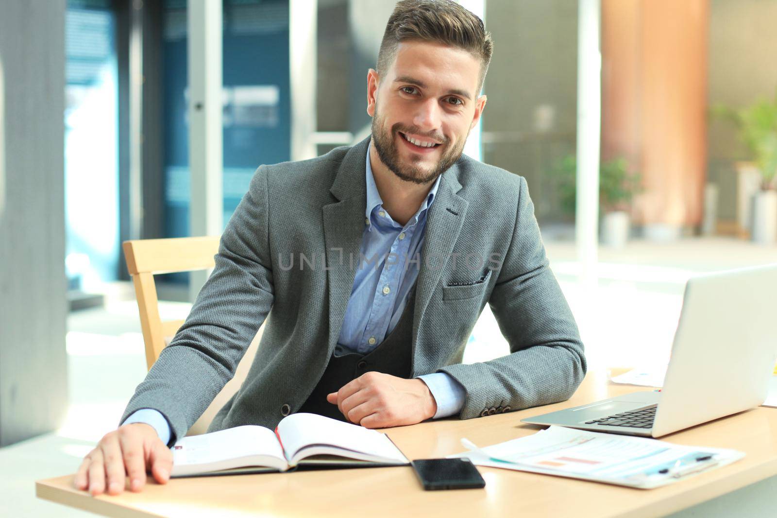 Portrait of happy businessman sitting at office desk, looking at camera, smiling. by tsyhun