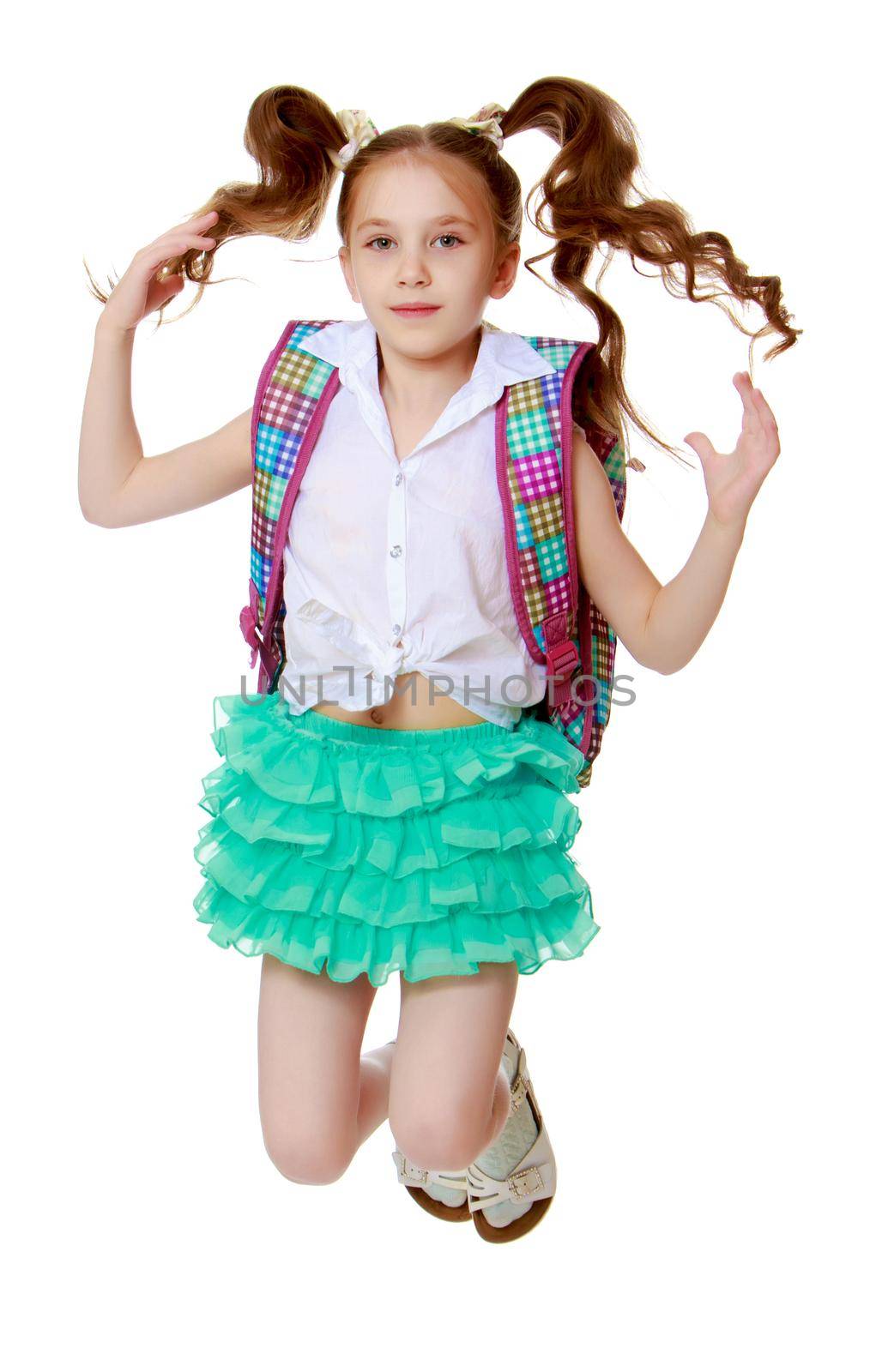Joyful little girl with long hair to the waist which wire braided white ribbons. In a white shirt without a pattern and green short skirt. Girl jumping with legs tucked under .