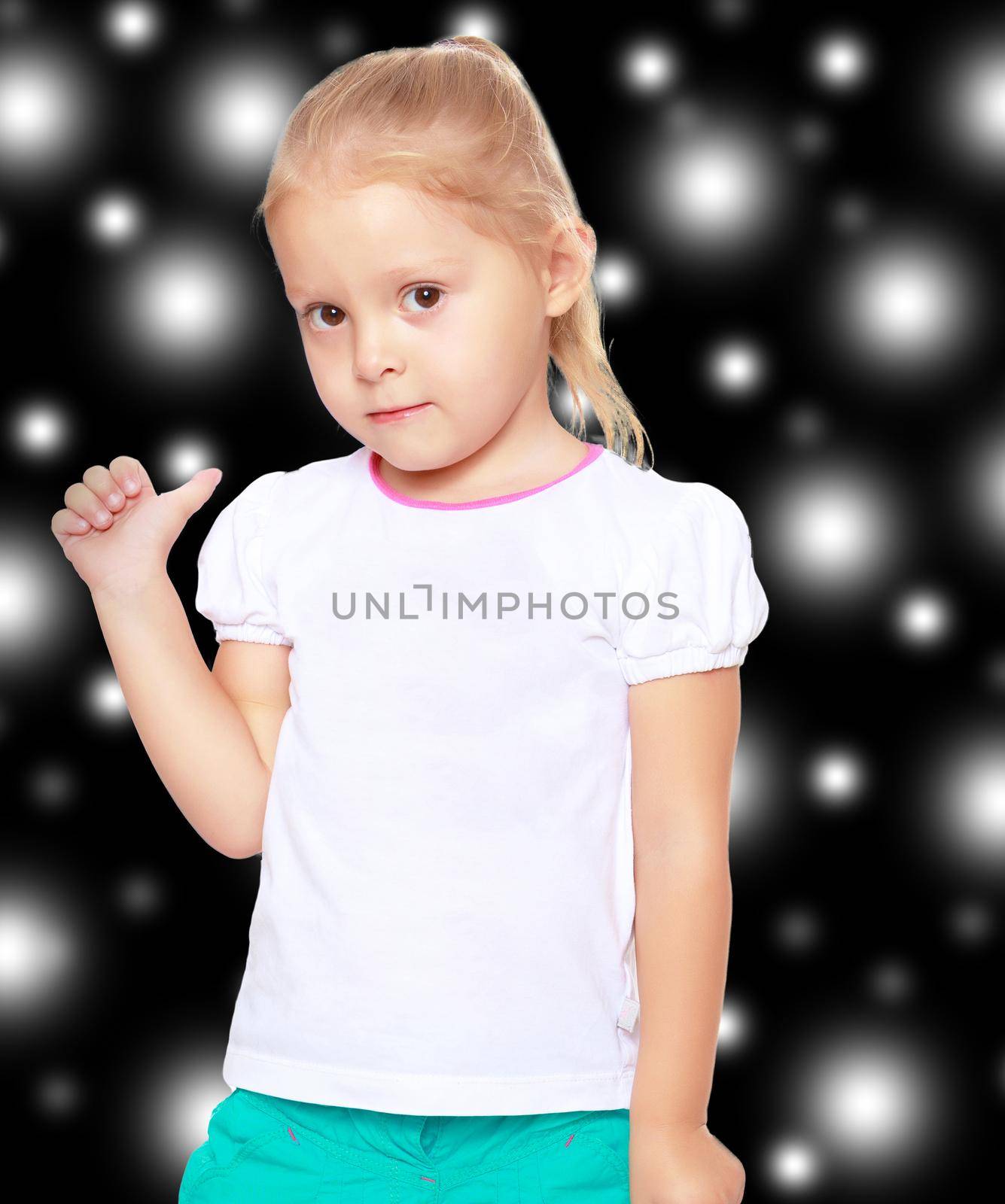 The concept of celebrating the New year, Holy Christmas, or child's birthday on a black background and white snowflakes.Cute little blond girl in white tank top without a pattern.Girl shows thumb to the side.
