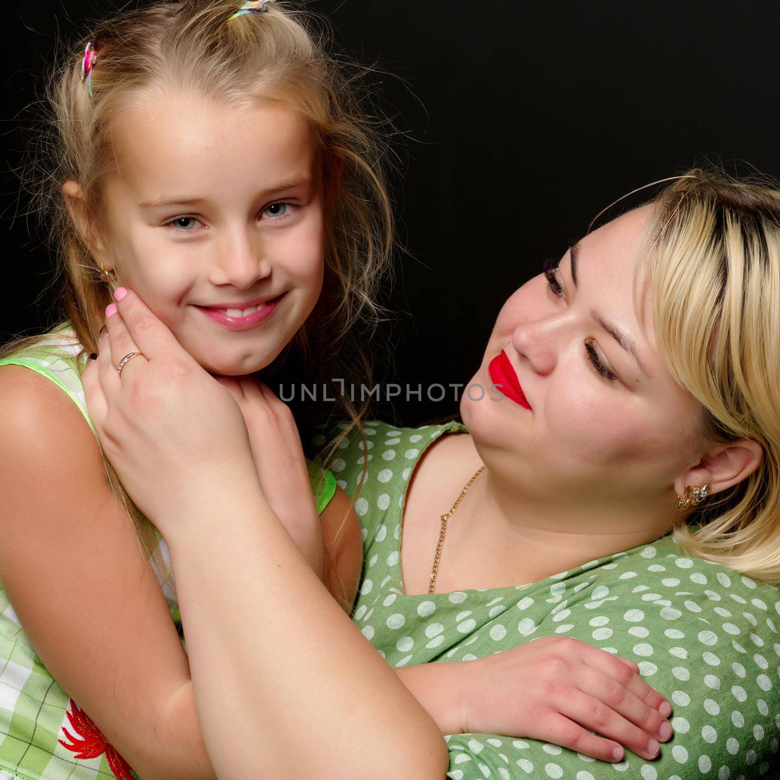 Happy family mom and daughter are hugging on a black background in the studio.