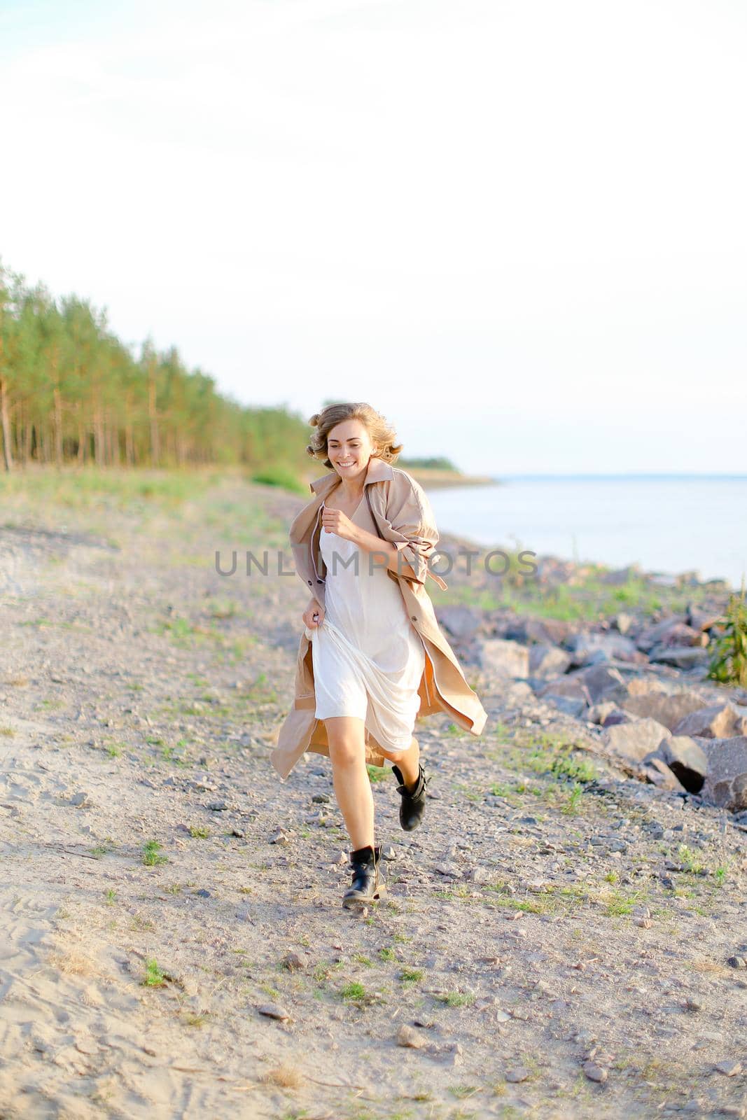 Caucasian pretty girl walking on shingle beach and wearing summer coat. Concept of seasonal fashion and summer vacations.