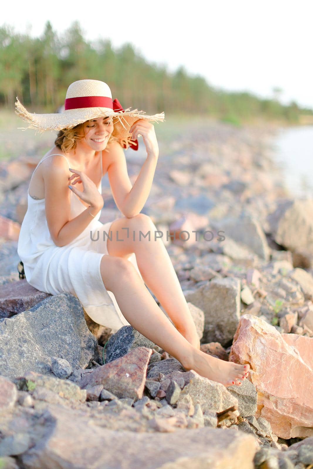 Young european woman in hat sitting on shingle beach. by sisterspro