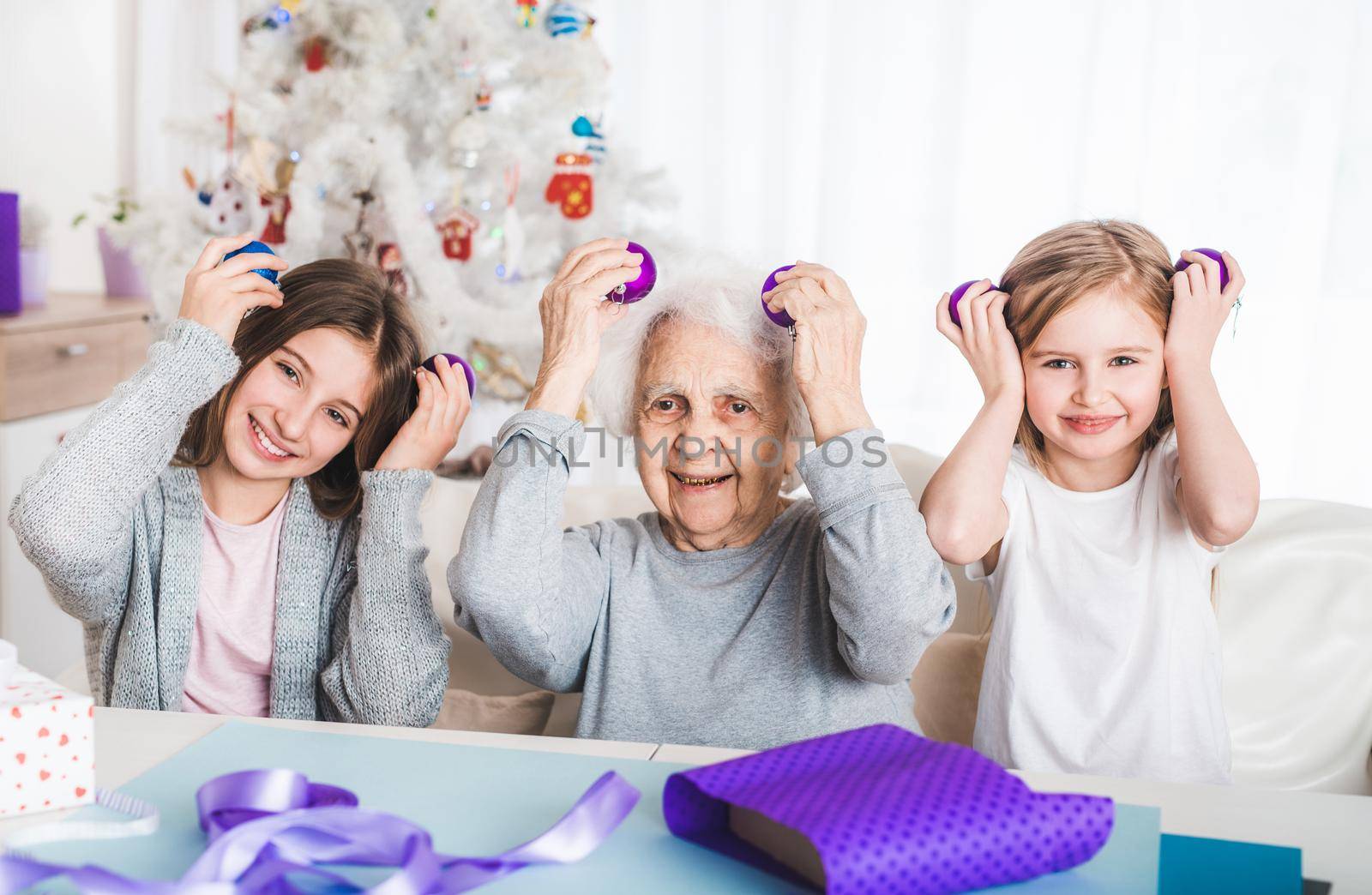 Smiling granddaughters holding decorative balls like eyes with grandma at Christmas