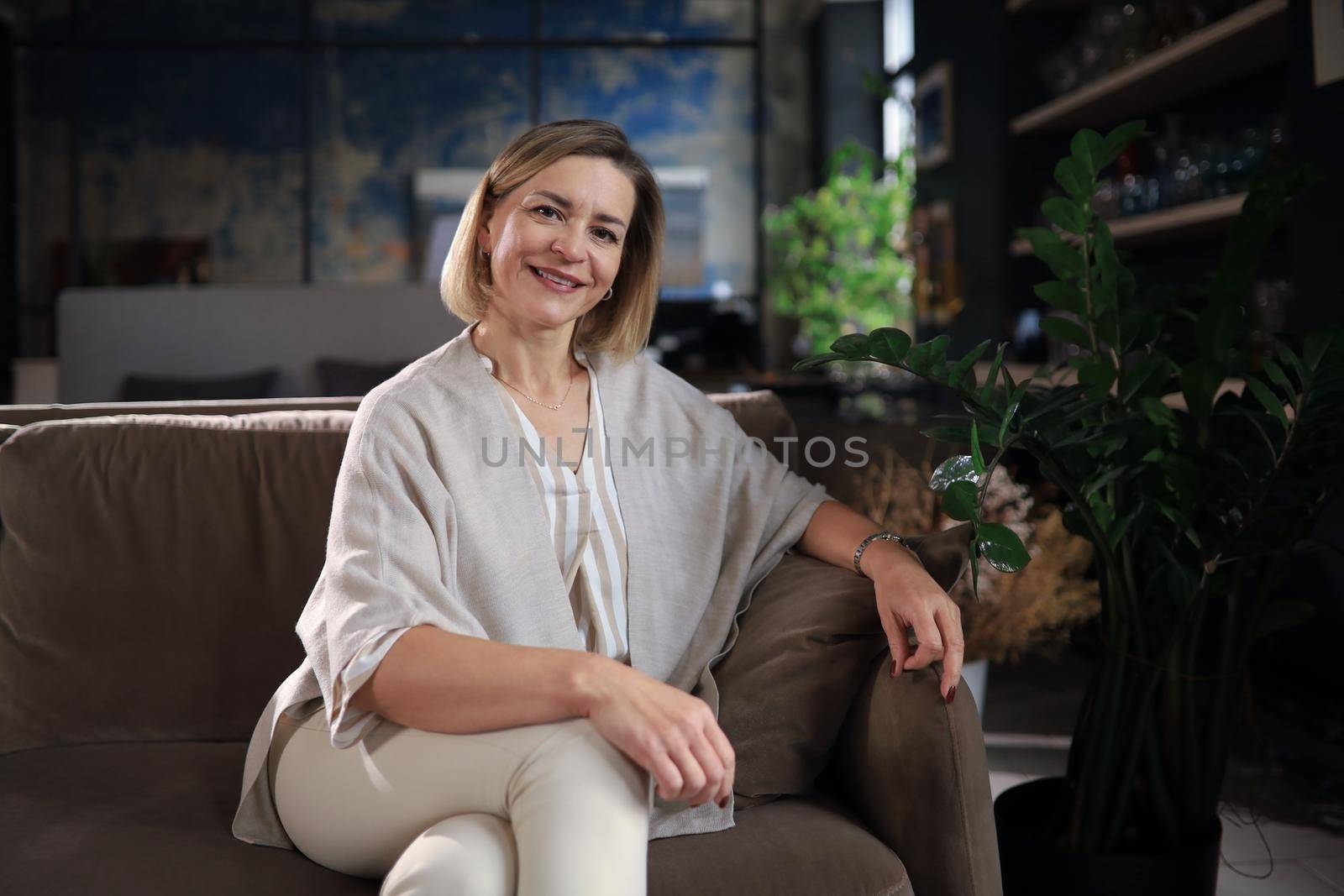 Beautiful blond middle aged woman relaxing sitting on sofa.