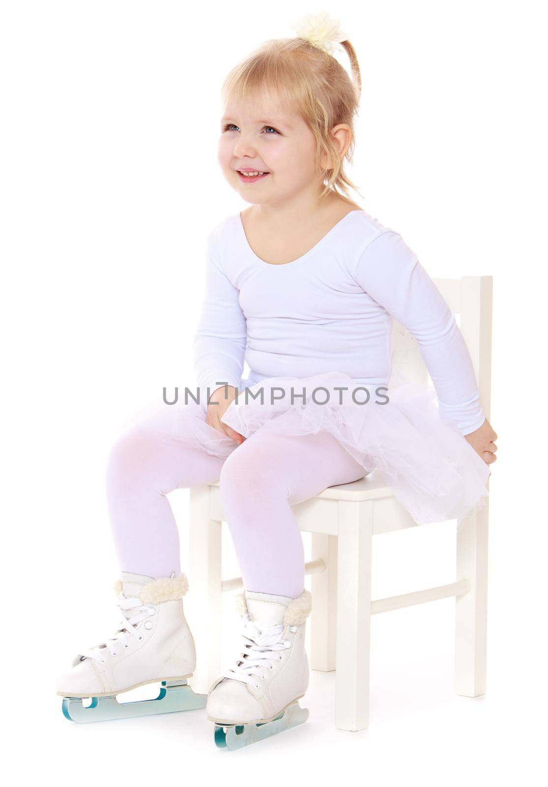 Cute little girl , a future figure skater, sits on a chair in a White sports dress and figure skates on two skids-Isolated on white background