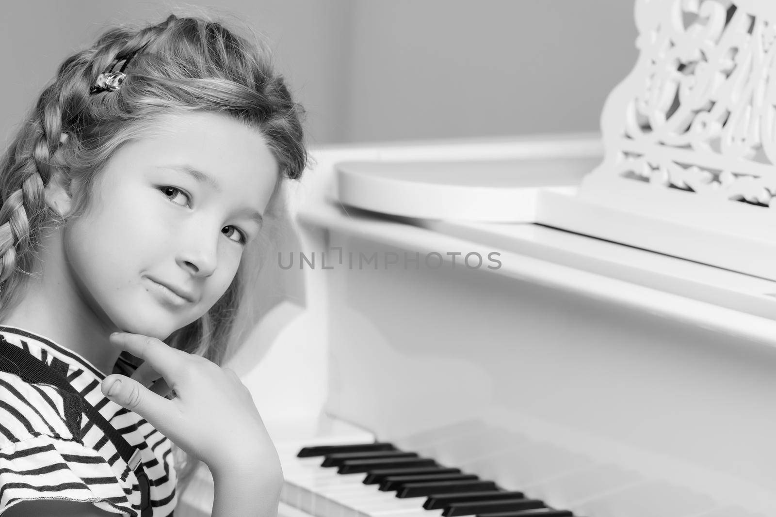 Beautiful little girl is playing the piano, retro style, black and white photo in the studio. The concept of music education, children's emotions.
