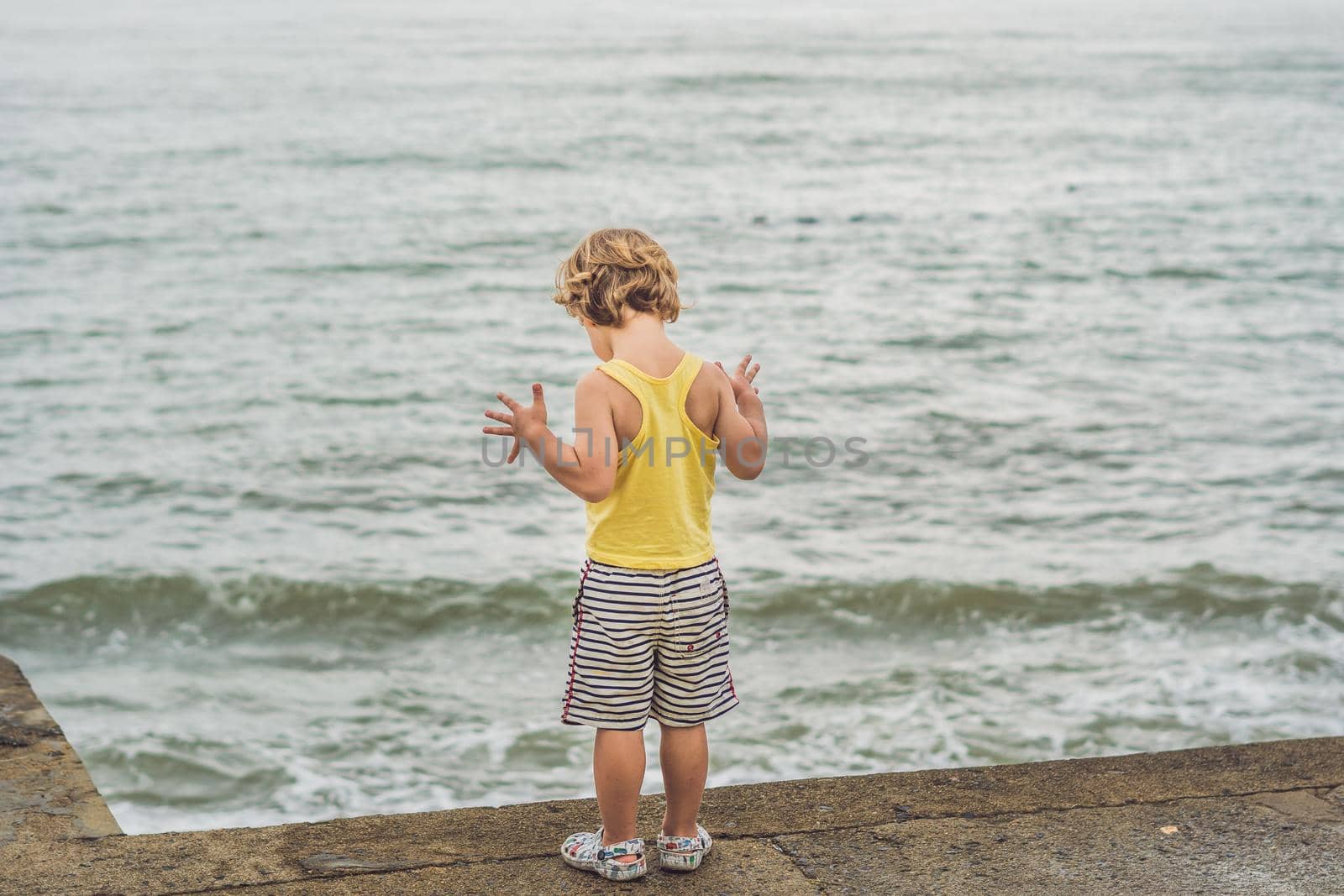 Cute boy stands on the shore watching the ocean waves by galitskaya