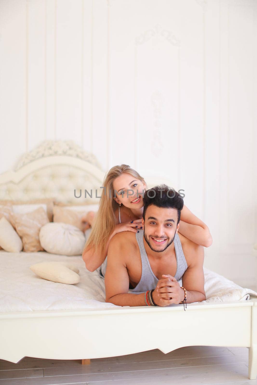 Blonde happy girl and hispanic biy lying in bad in morning. Concept of happy couple and resting on weekends in bedroom.