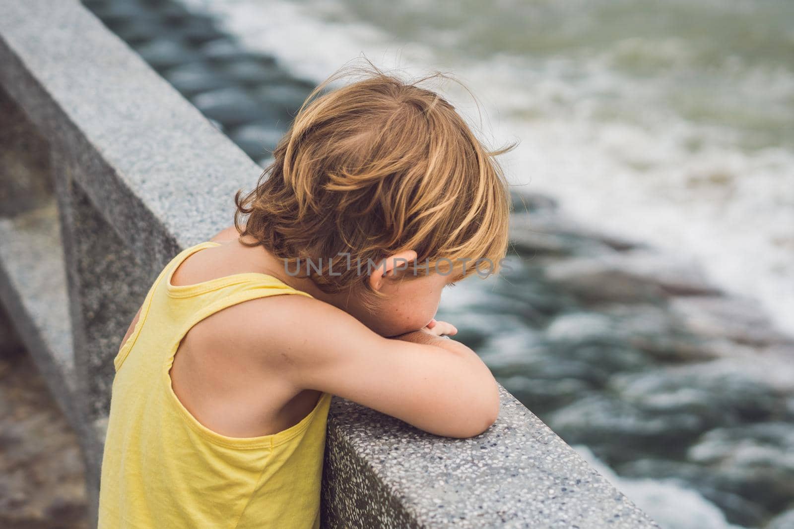 Cute boy stands on the shore watching the ocean waves.
