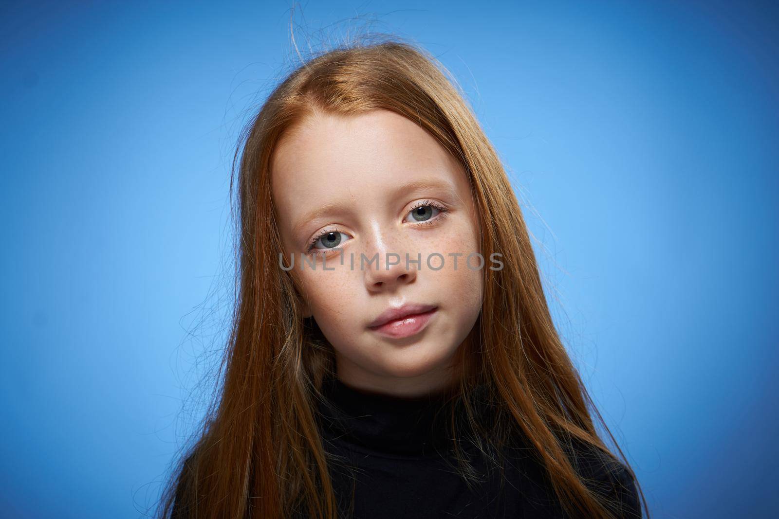 redhead girl with freckles on her face posing close-up blue background. High quality photo