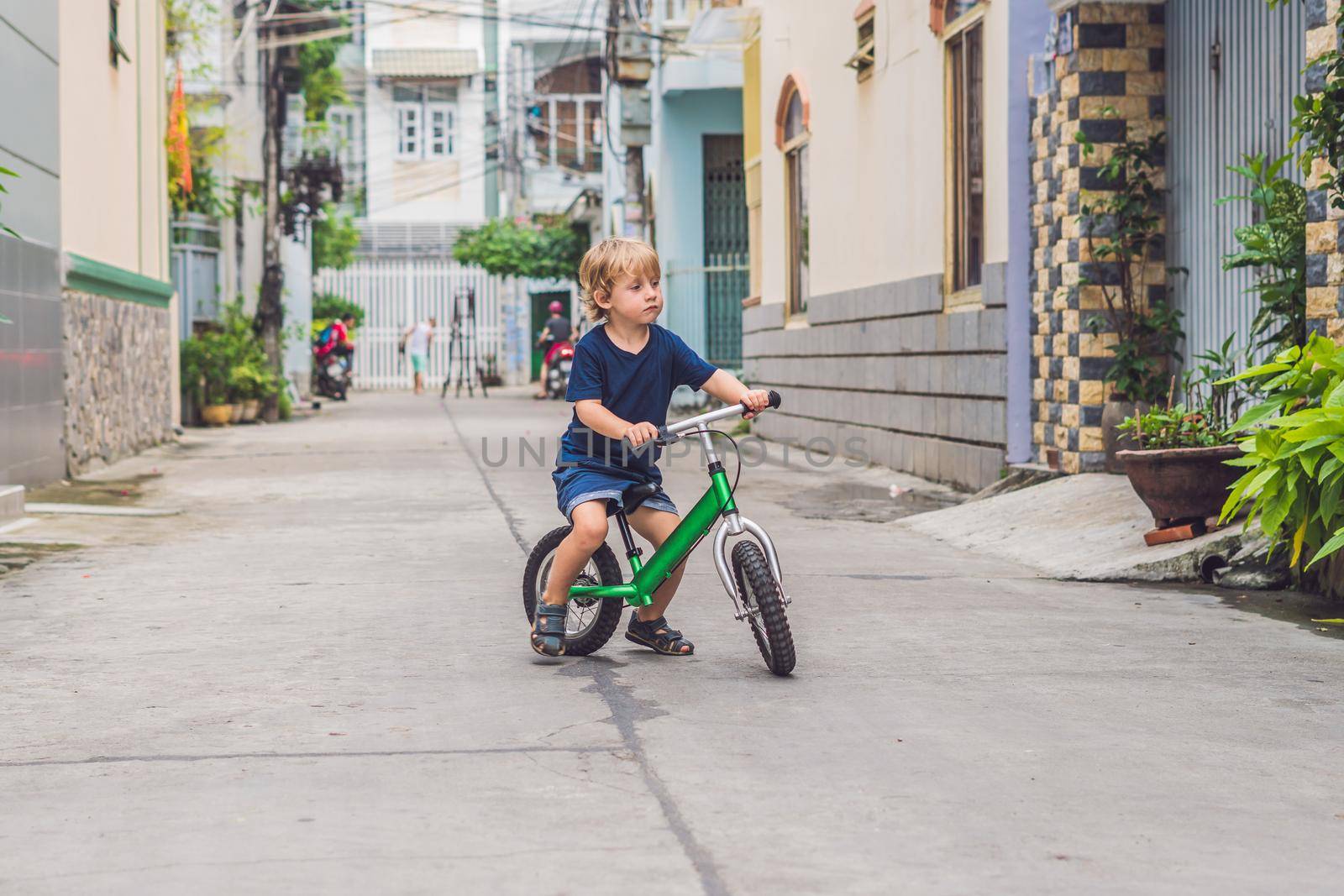 Active blond kid boy driving bicycle n the street of the city. Toddler child dreaming and having fun on warm summer day. outdoors games for children. Balance bike concept.