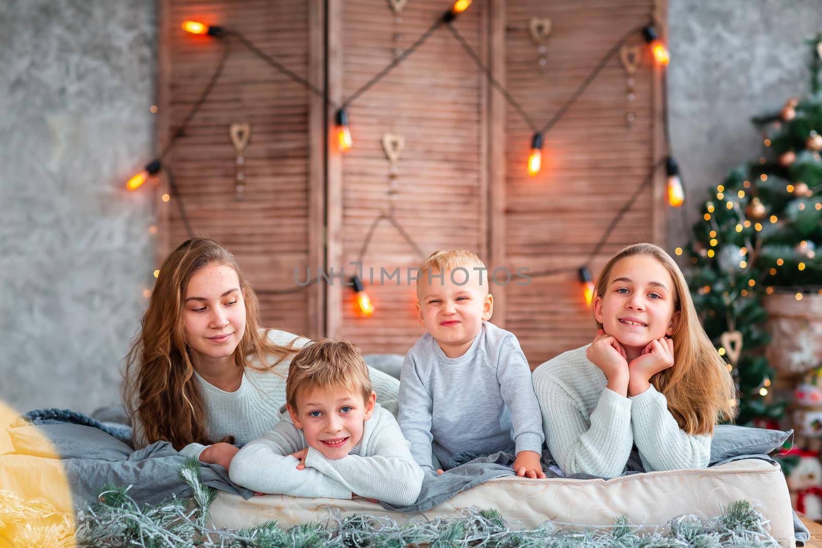 Happy kids siblings having fun on the bed near the Christmas tree on Christmas morning by Len44ik