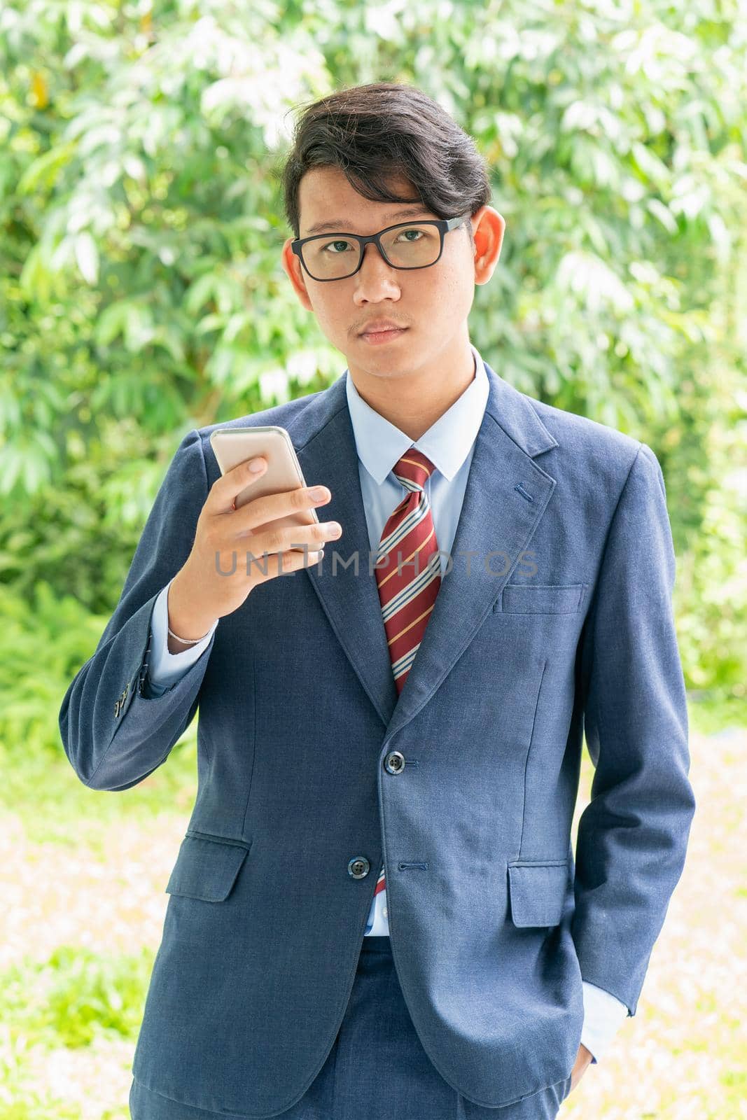 Young asian business men portrait in suit and wear eyeglasses standing outside in a park during sunny day