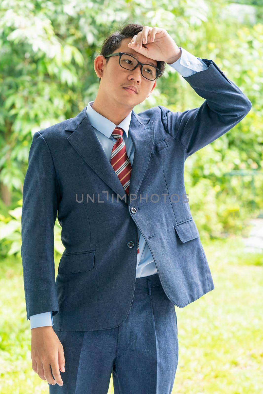 Young asian business men portrait in suit and wear eyeglasses standing outside in a park during sunny day