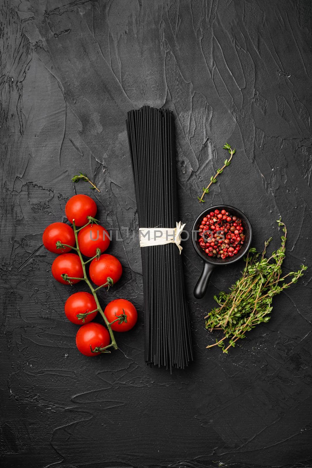 Black colored spaghetti raw dry set, on black dark stone table background, top view flat lay, with copy space for text