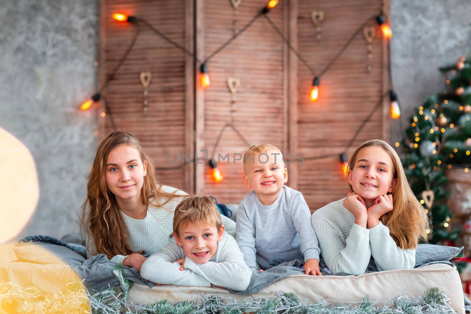 Happy kids siblings having fun on the bed near the Christmas tree on Christmas morning by Len44ik