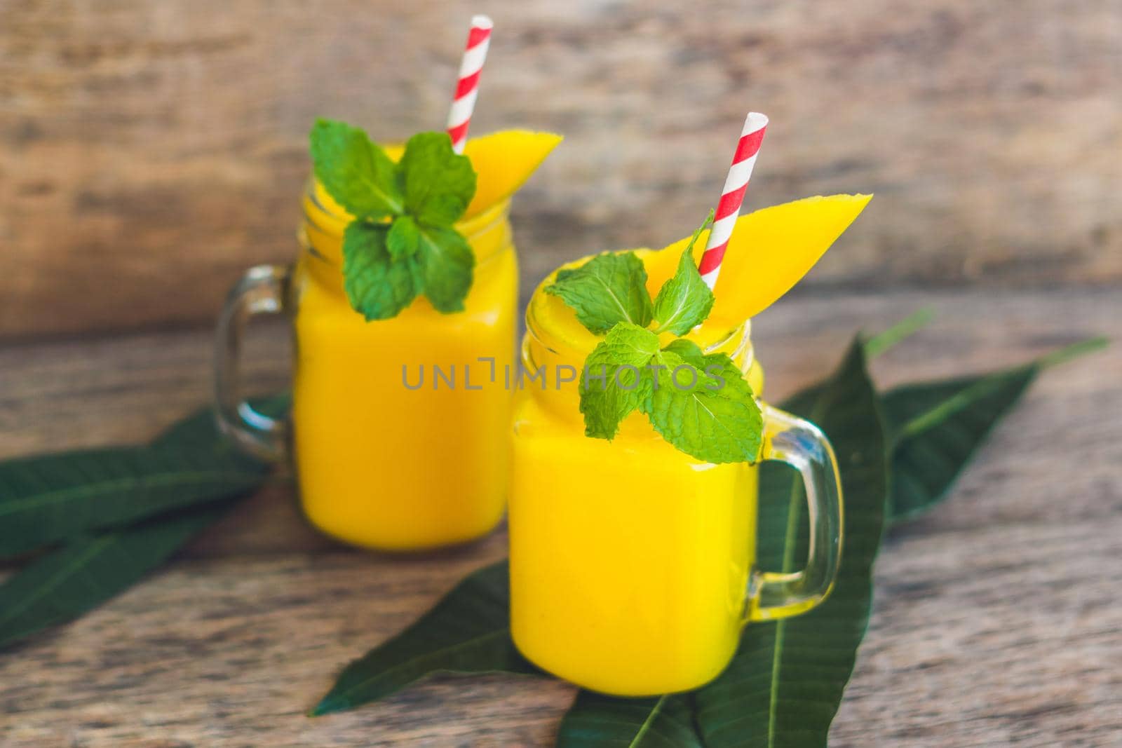 Juicy smoothie from mango in two glass mason jars with striped red straw on old wooden background. Healthy life concept, copy space.
