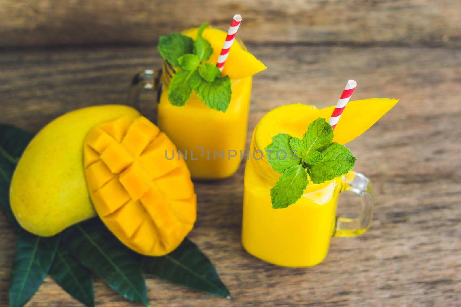 Juicy smoothie from mango in two glass mason jars with striped red straw on old wooden background. Healthy life concept, copy space.