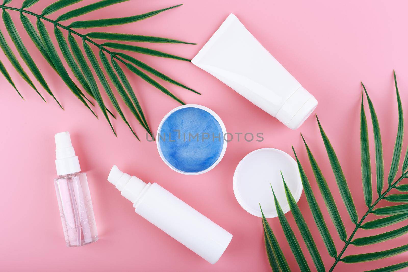 Creative flat lay with cosmetic products for cleaning, moisturizing and exfoliating skin on pink background with palm leaves. Concept of organic natural beauty products for daily skin care