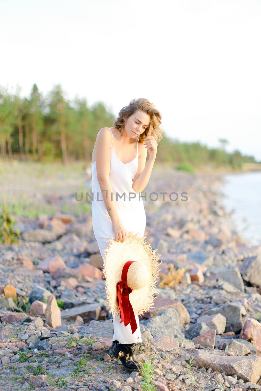 Caucasian girl walking on shingle beach with hant in hands and wearing dress. Concept of summer vacations and fashion.