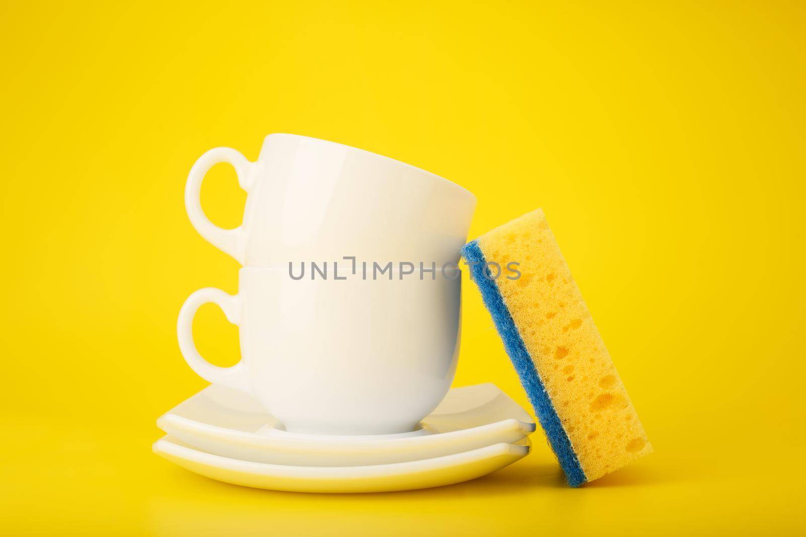 Dishwashing minimal concept. Plates, cups and cleaning sponge against bright yellow background by Senorina_Irina
