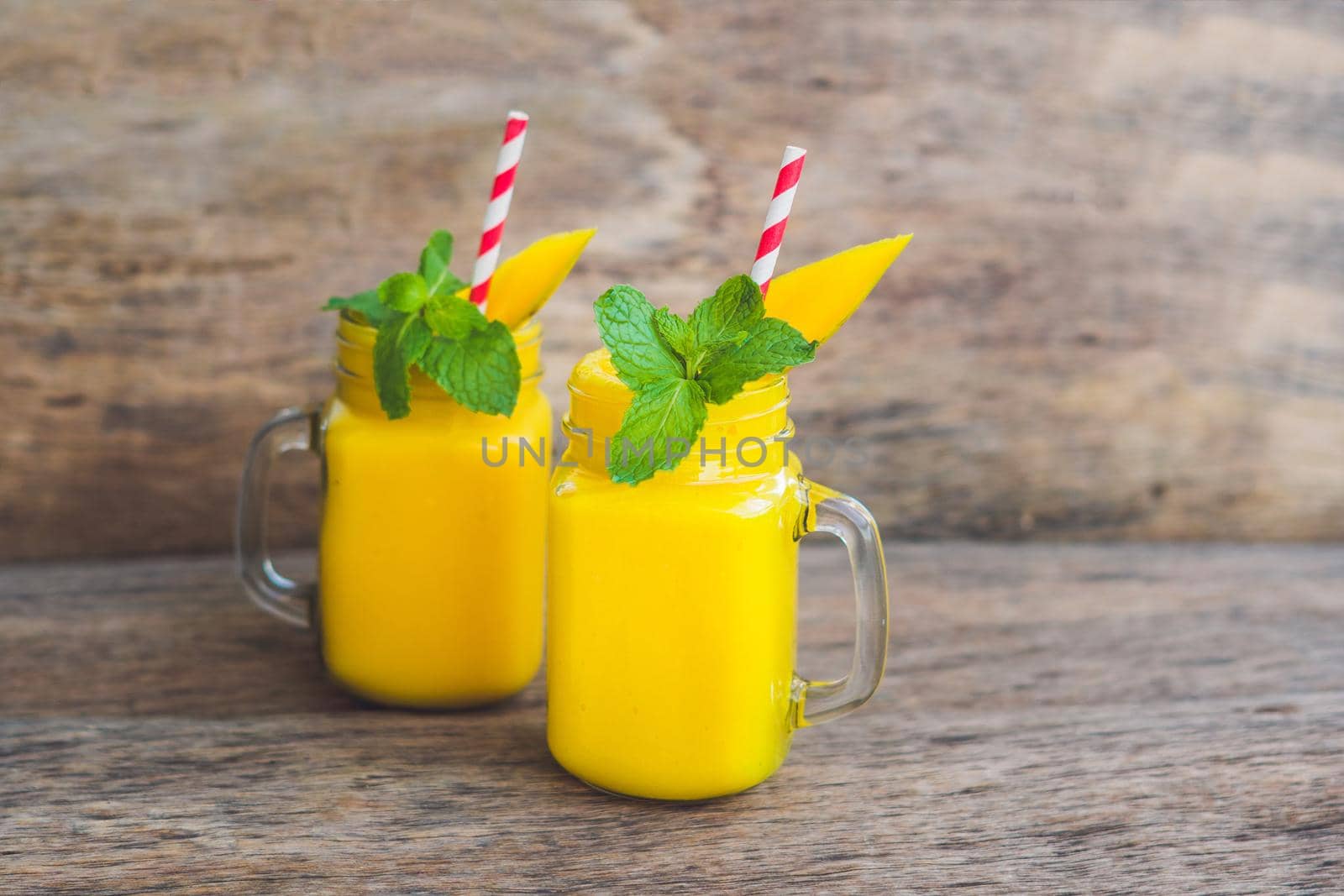 Juicy smoothie from mango in two glass mason jars with striped red straw on old wooden background. Healthy life concept, copy space by galitskaya