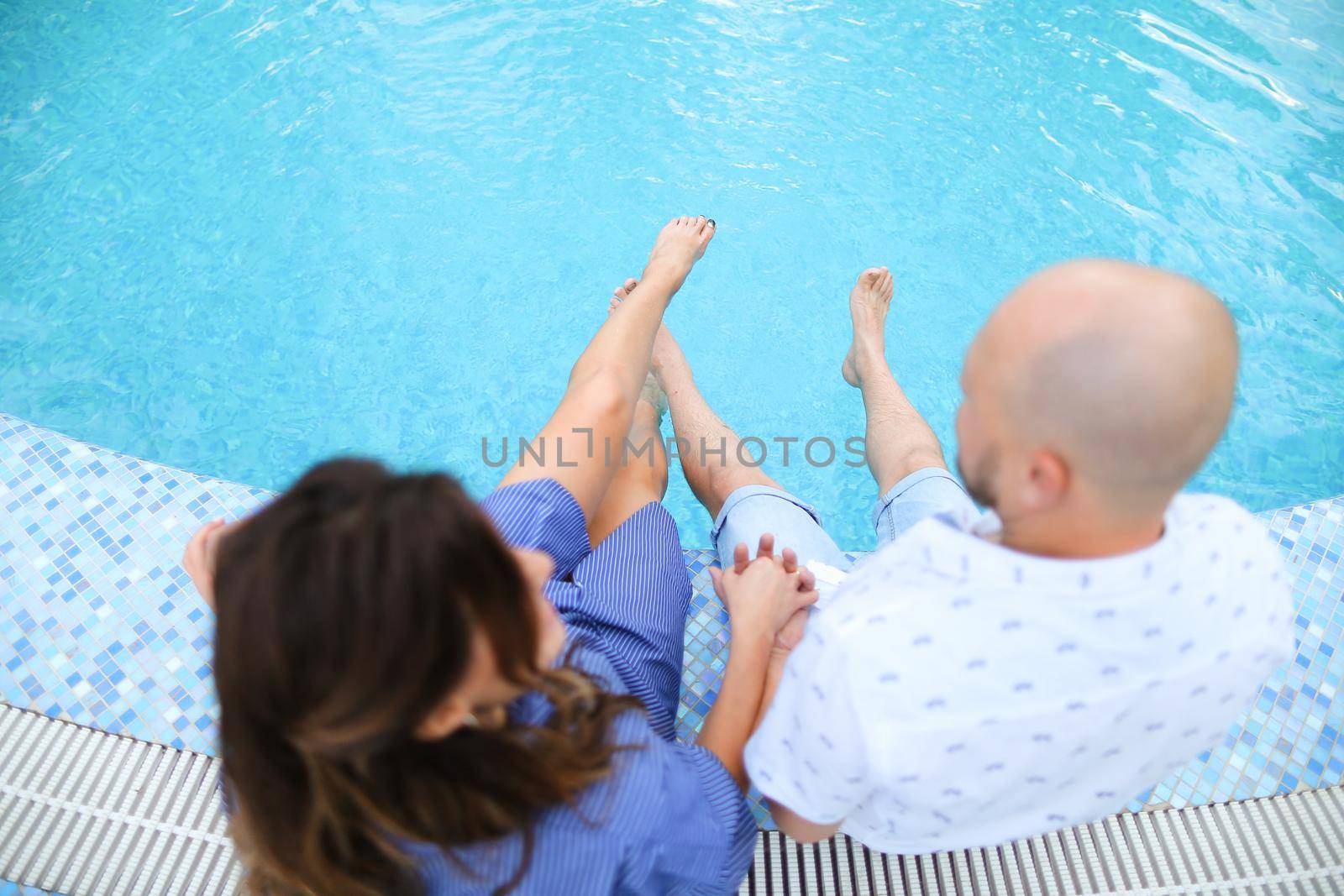 Husband and wife sitting barefoot near swiming pool. Concept of happy couple and summer vacations on resort.