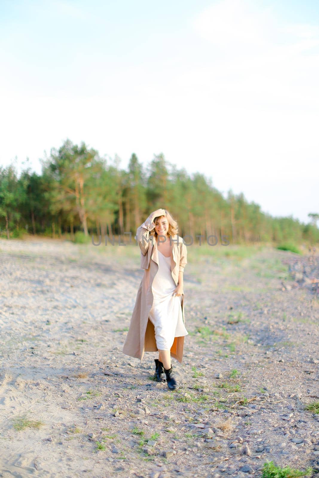 Caucasian nice girl walking on shingle beach and wearing summer coat. Concept of seasonal fashion and summer vacations.