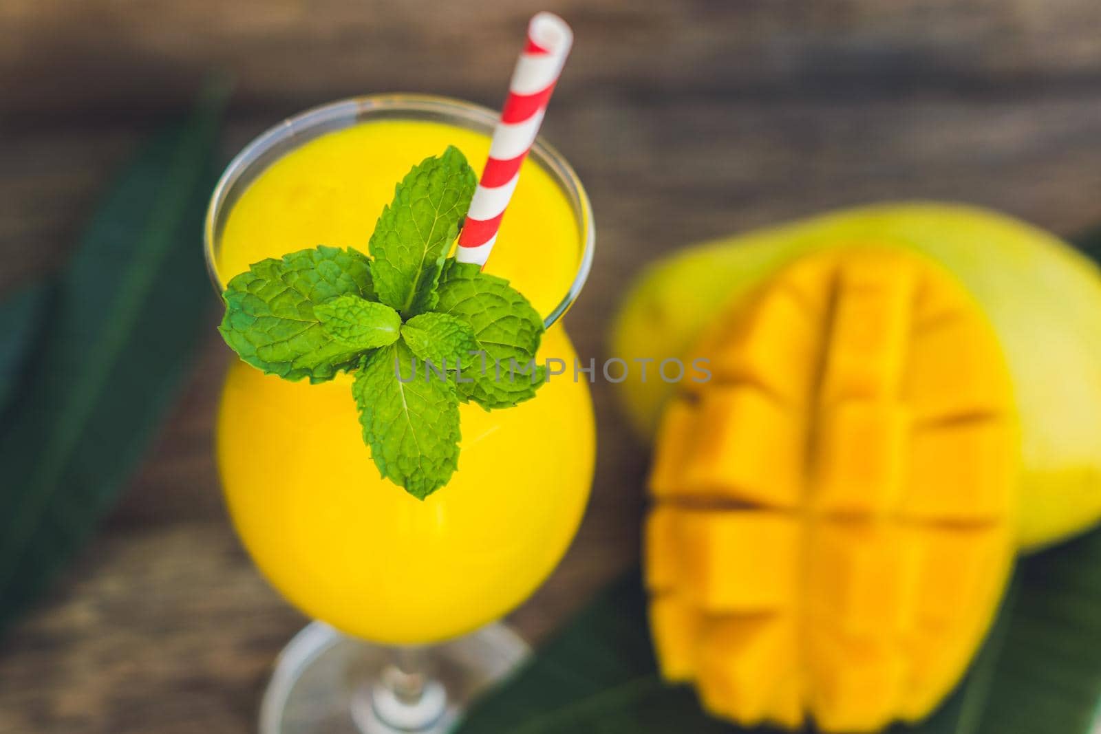 Juicy smoothie from mango in glass with striped red straw and with a mint leaf on old wooden background. Healthy life concept, copy space by galitskaya