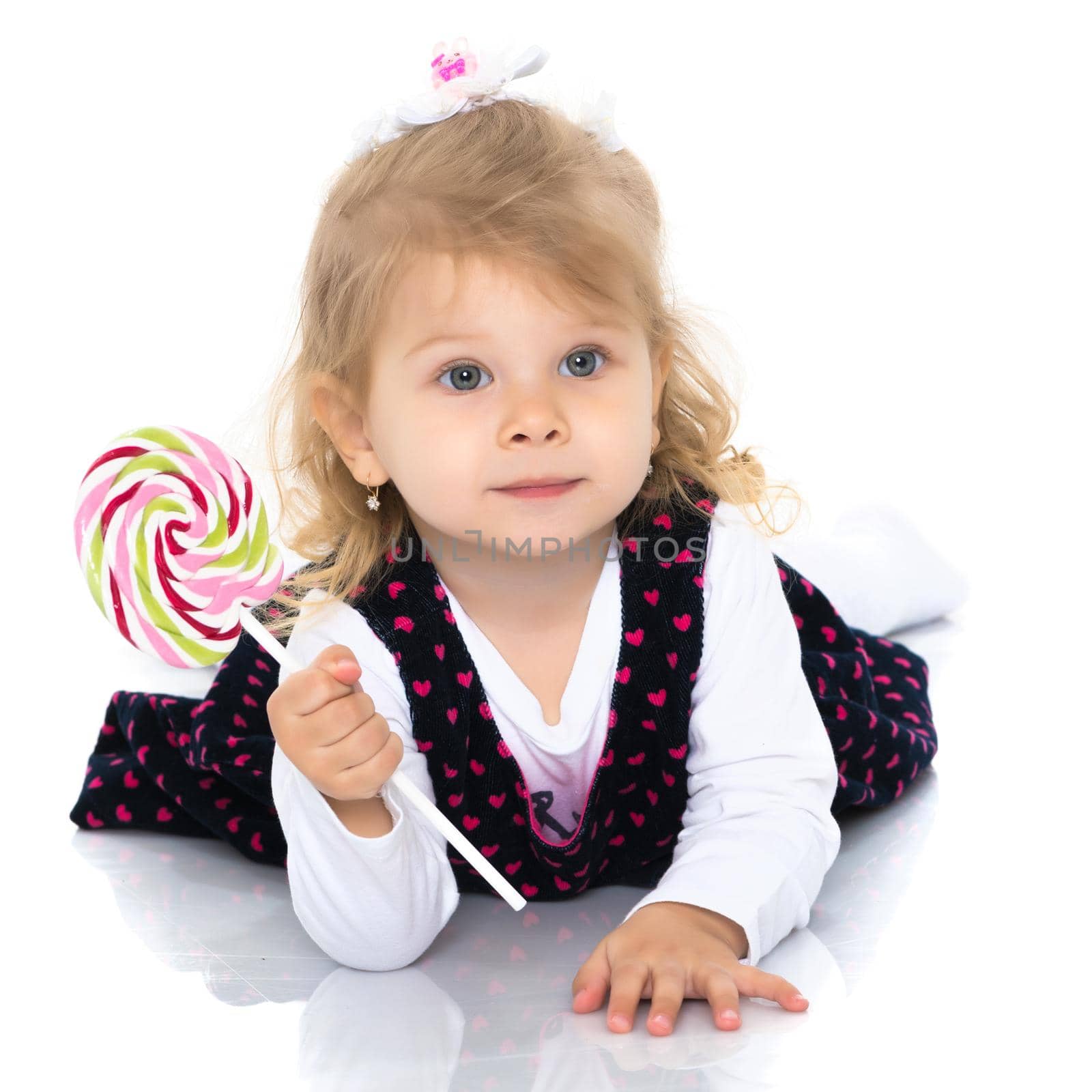 A little girl licks a candy on a stick. The concept of a happy childhood, proper nutrition. Isolated on white background.