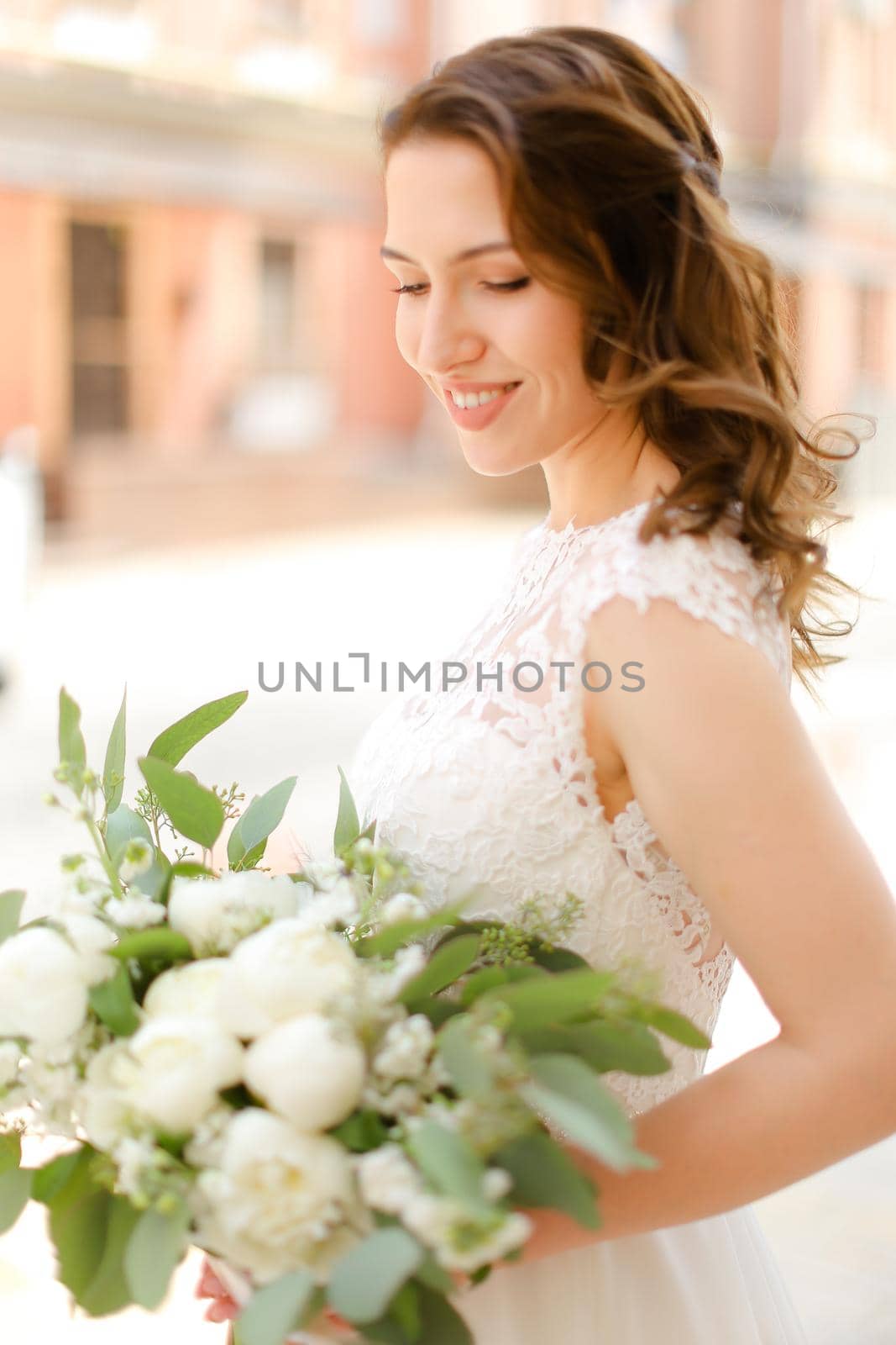 Happy pretty fiancee keeping bouquet of flowers and wearing white dress. Concept of bridal photo session and wedding.