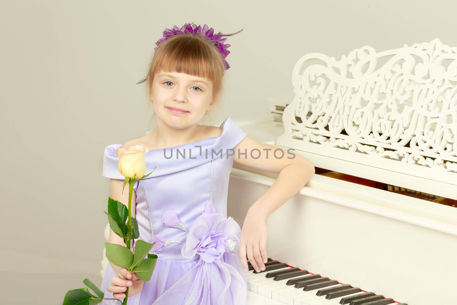 Fashionable little girl in a stylish beautiful dress.The girl is playing on a large white piano.He holds a rose in his hand.