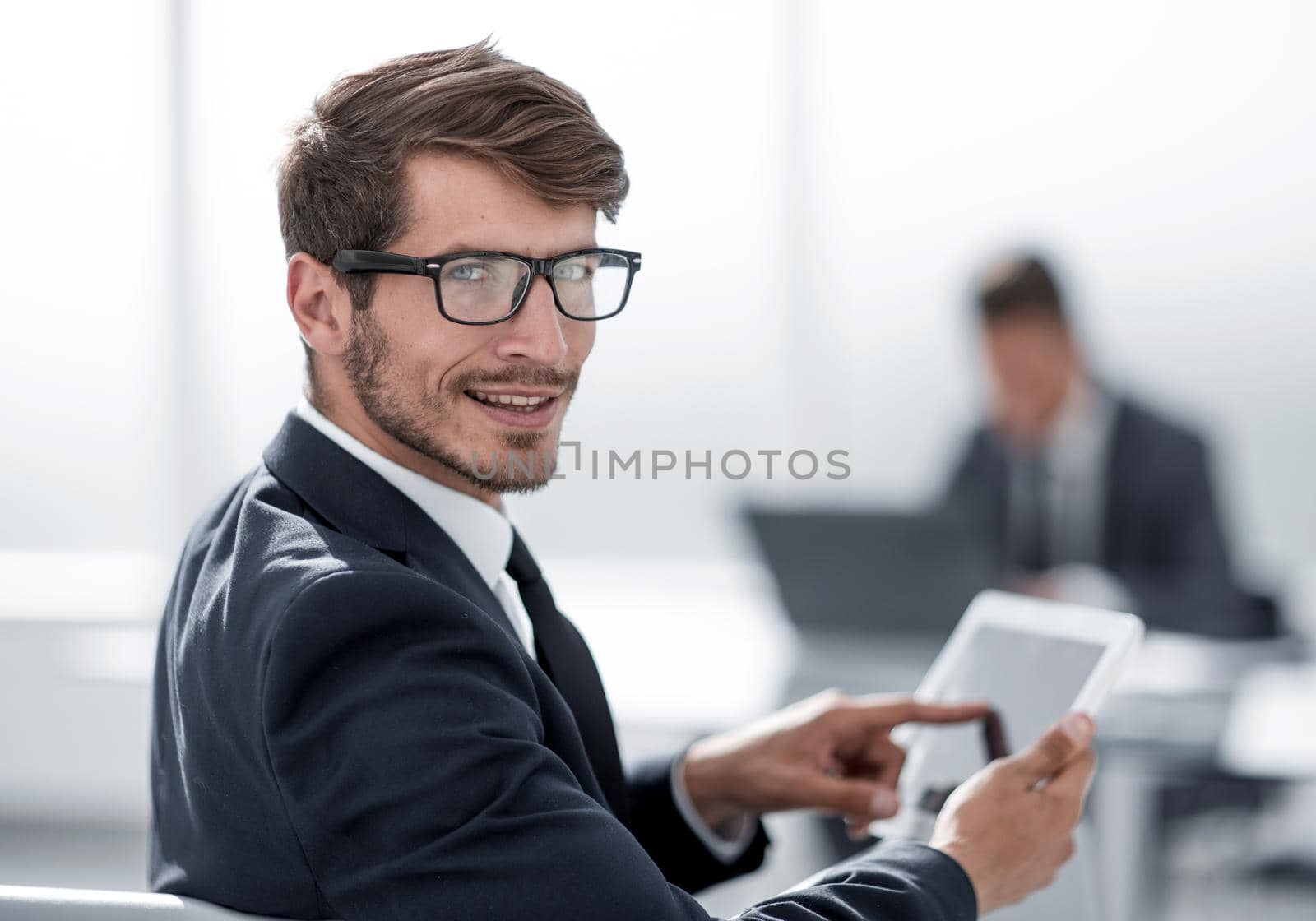young man with glasses looks at camera and smiles using tablet
