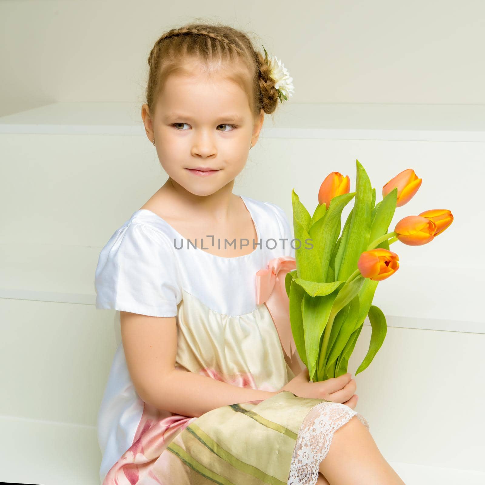 A cute little girl with a bouquet of tulips, in the spring in the studio. The concept of the awakening of nature after winter, the expectation of summer.