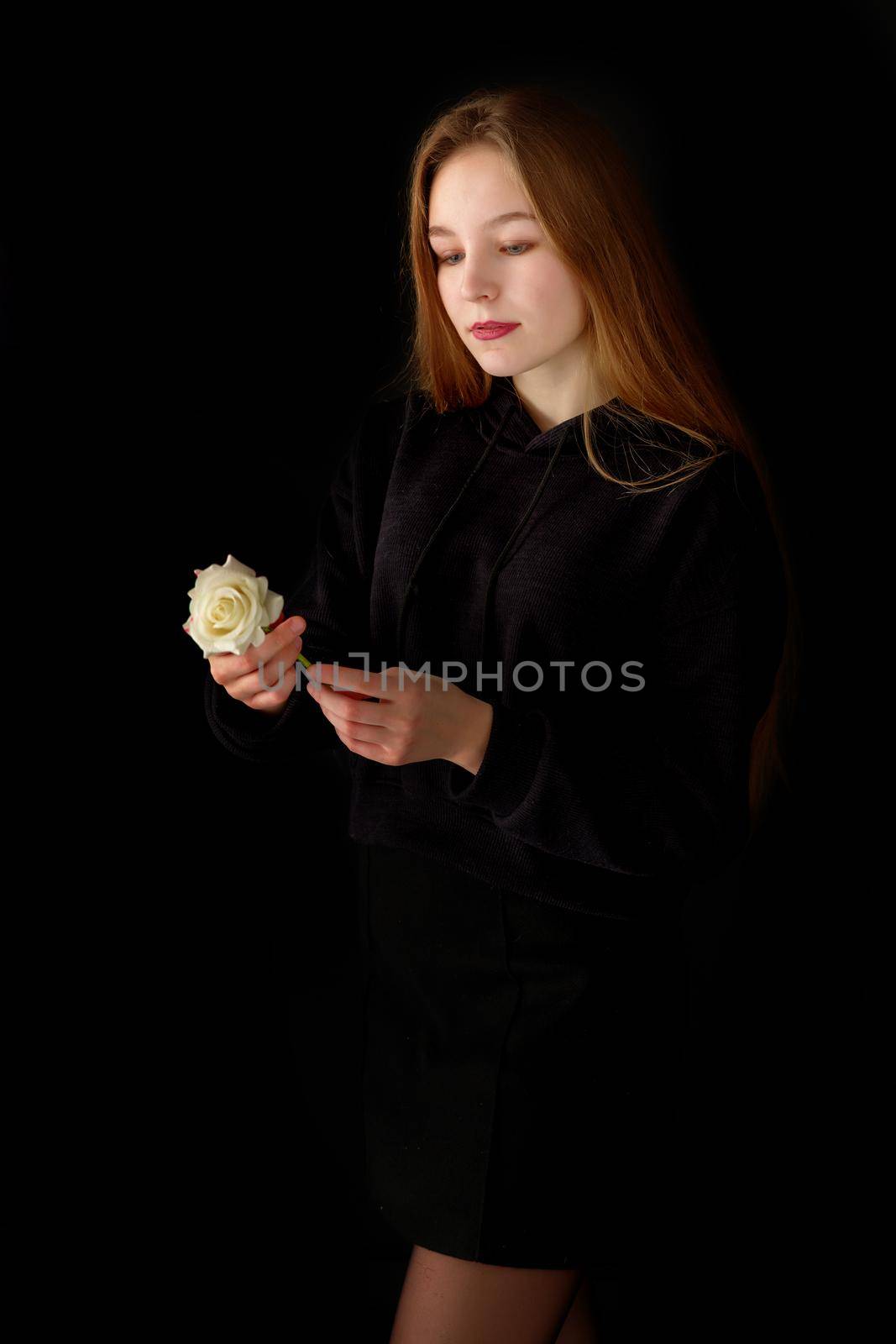 Beautiful little girl with a flower in her hand. The concept of style and fashion. On a black background.